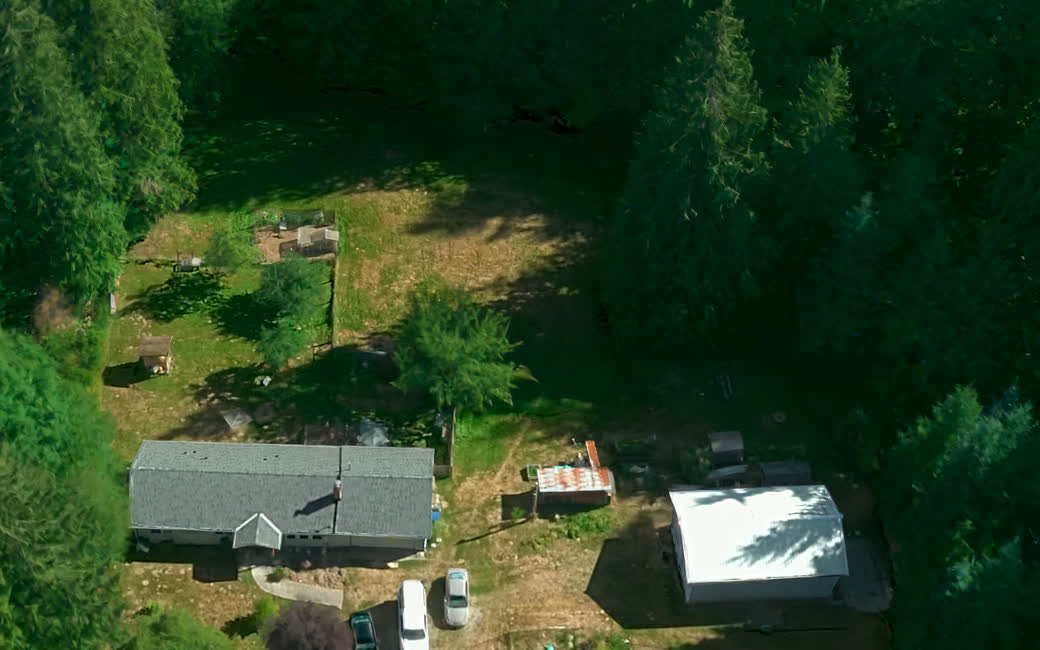 An overhead aerial view of the property showing the house, the shop, the deck, the driveway and the ground around them.