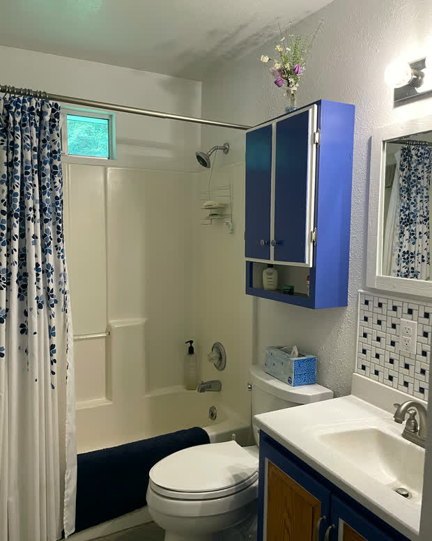 The bathroom: a tub with a tiled surround, a vanity, a toilet and a tiled floor.