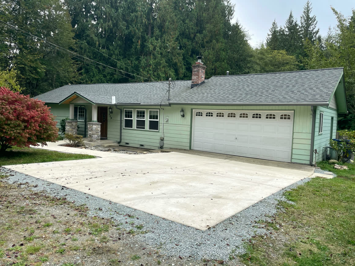 The front of the house with a white double overhead garage door and a broad concrete parking apron in front of it.