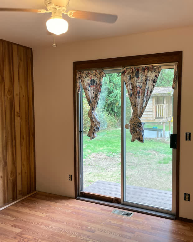 The living room: a knotty-pine panelled wall, hardwood floor, a ceiling fan and a sliding glass door opening onto the deck.