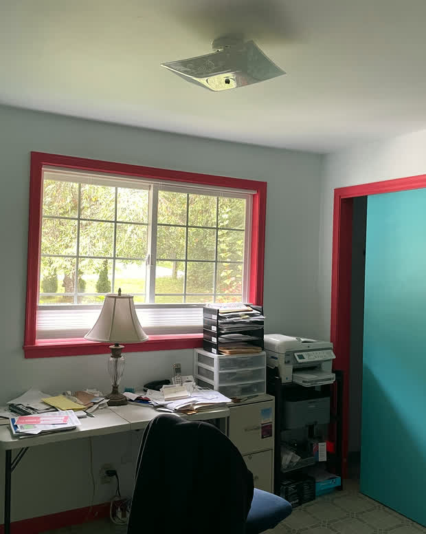A second room with closets, currently used as an office, with a red-trimmed window.